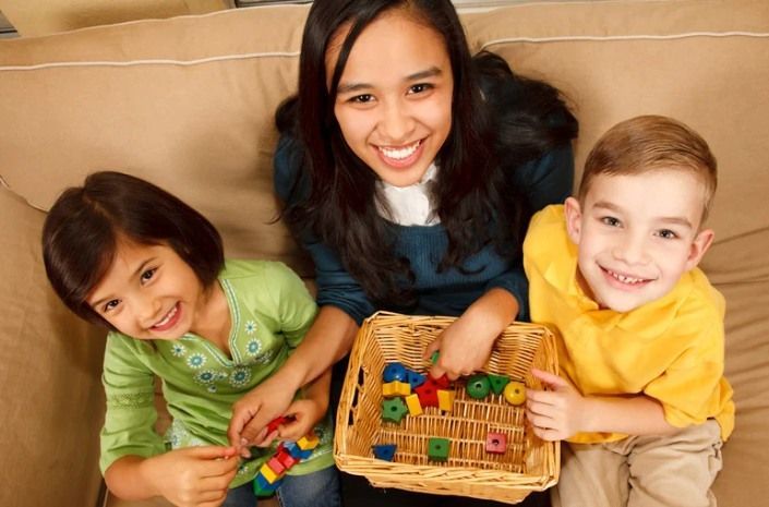 Woman and two children smiling while playing with colorful blocks in a basket.