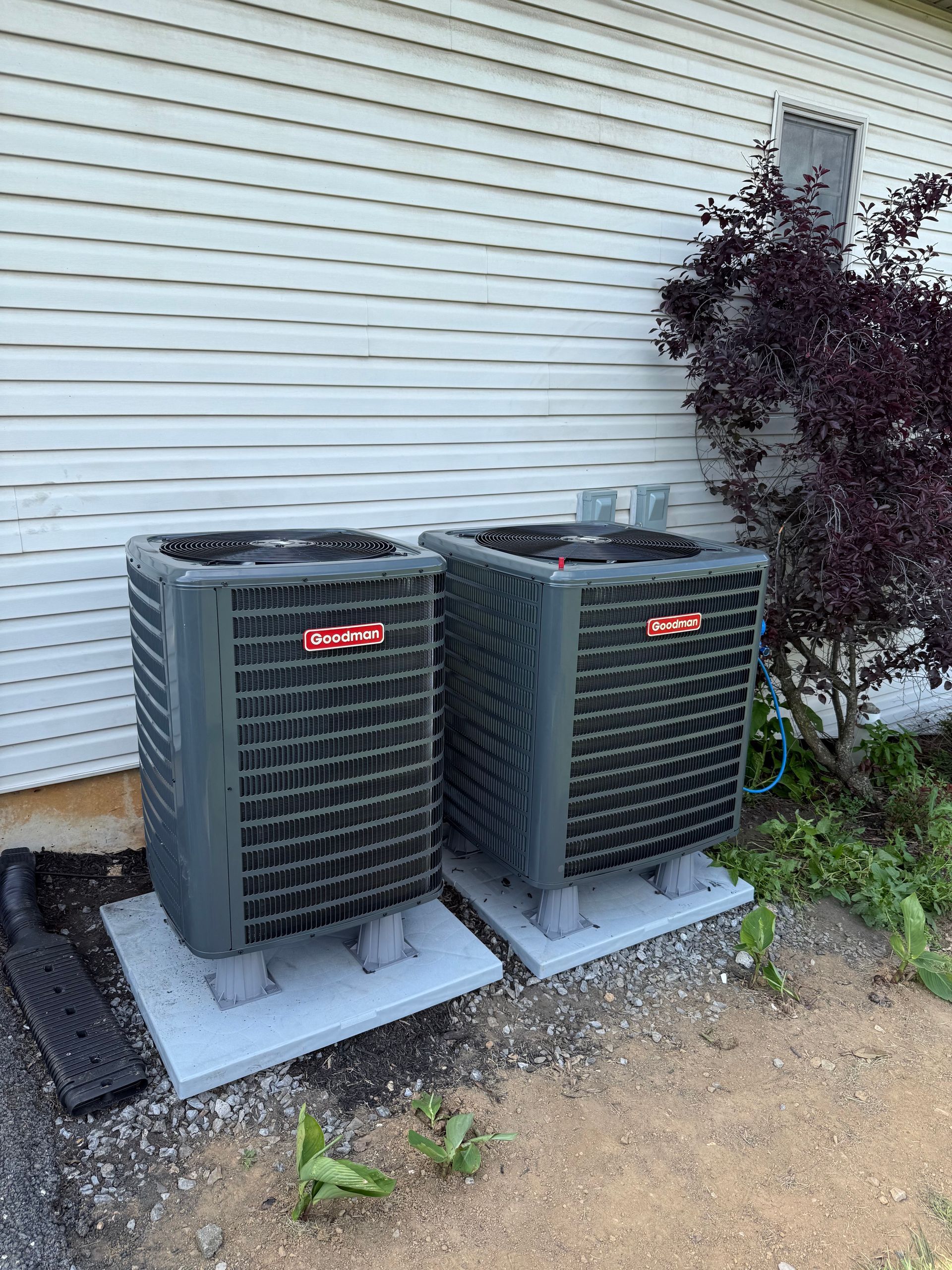 Two air conditioners are sitting next to each other in front of a house.