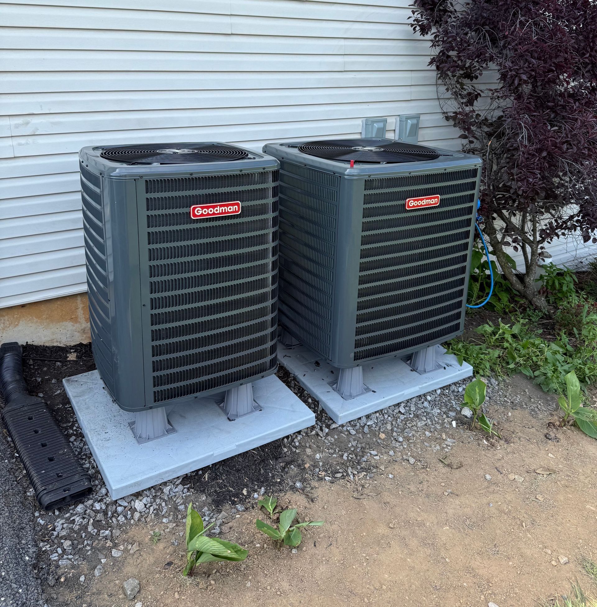 Two air conditioners are sitting next to each other in front of a house.