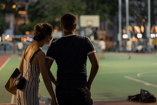 Couple watching a nighttime basketball game together at an outdoor court