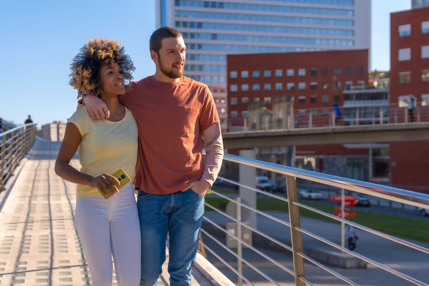 Couple walking together on a sunny day across a modern city bridge
