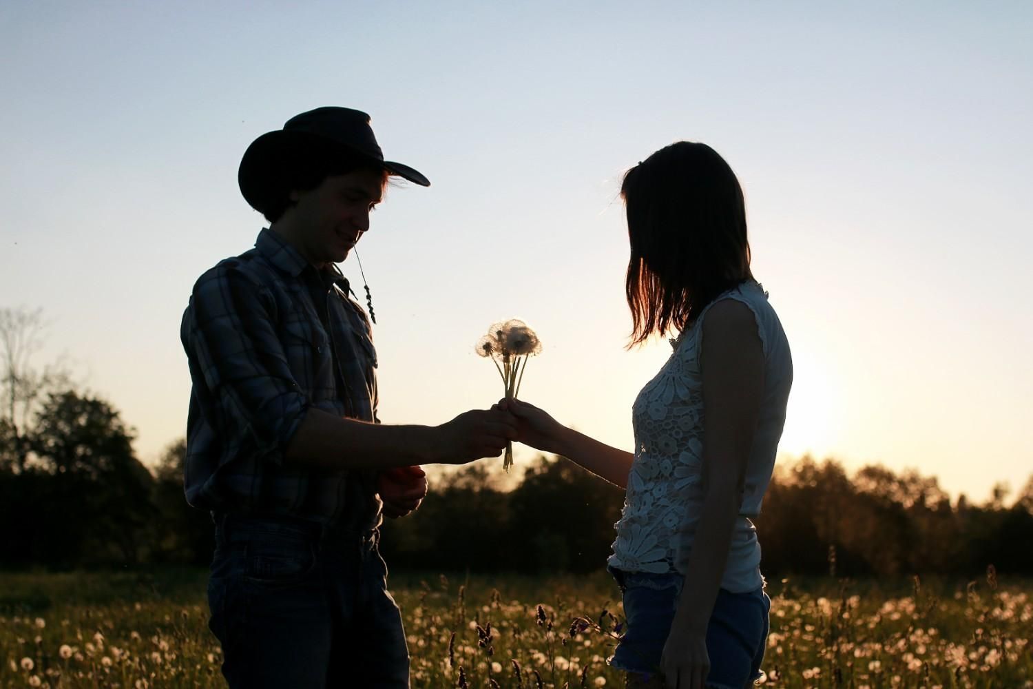 Man in a cowboy hat giving flowers to a woman at sunset in a peaceful field