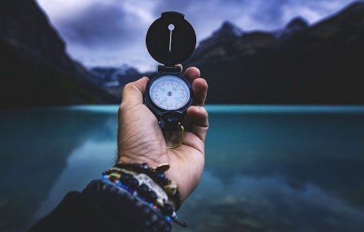 Hand holding a compass while overlooking a calm mountain lake, symbolizing finding direction