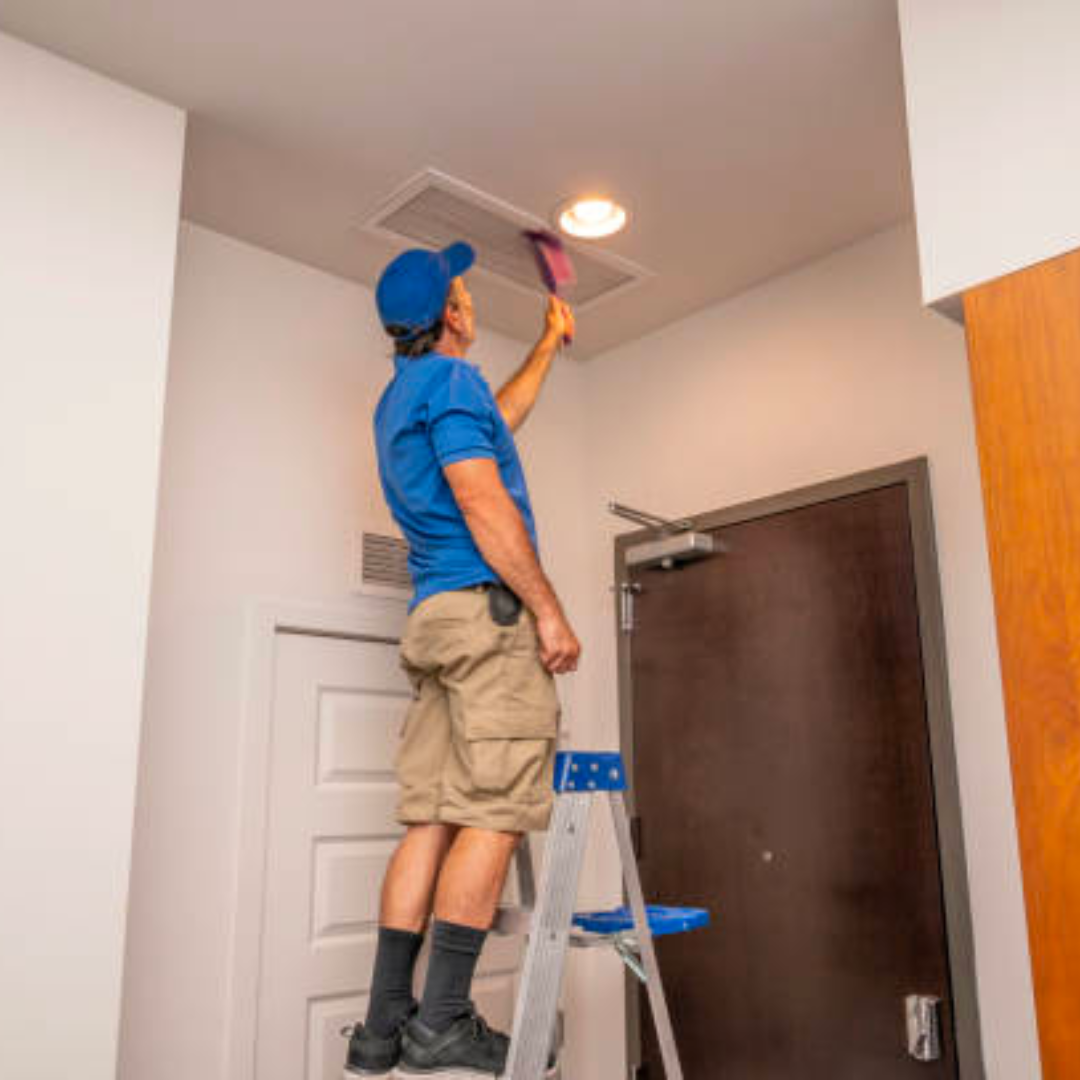 A man is standing on a ladder cleaning the ceiling.