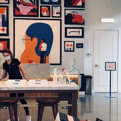 a woman wearing a mask is standing in front of a table in a room with paintings on the wall .