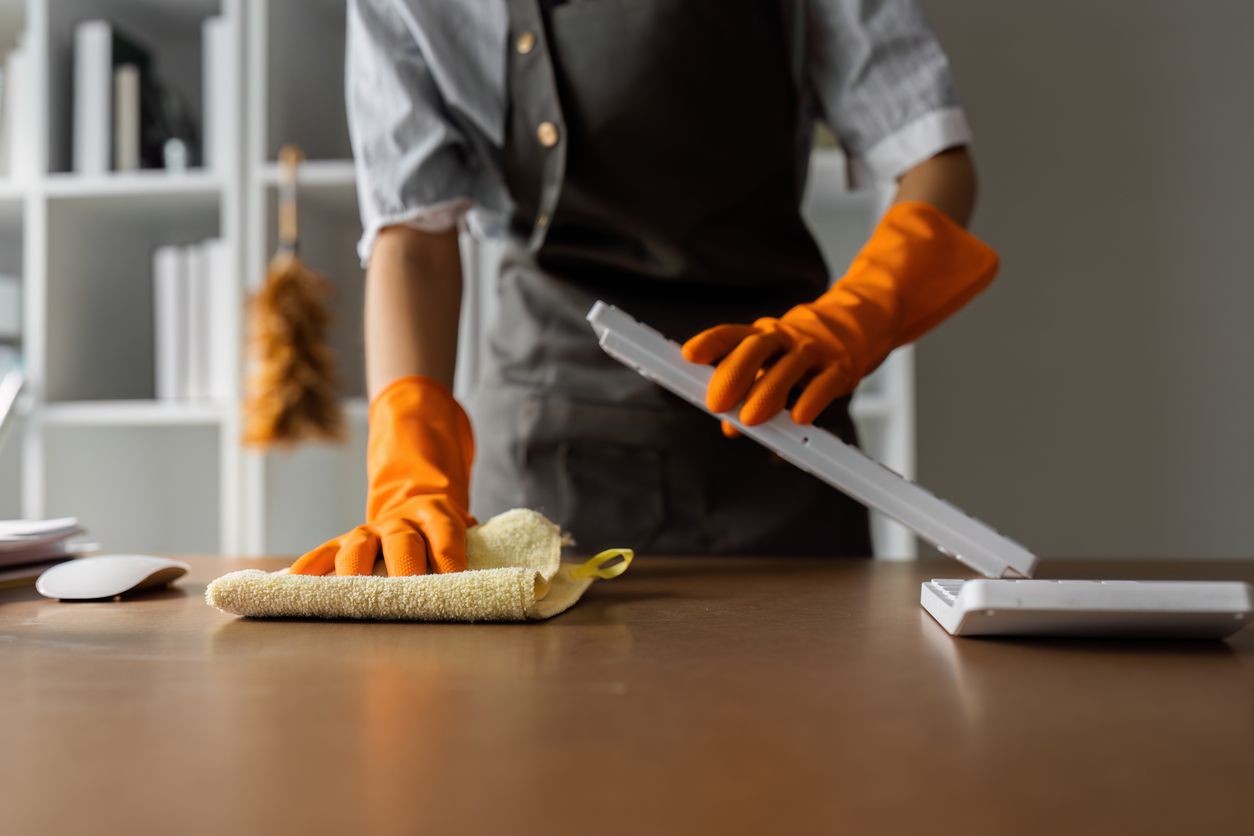 A person wearing orange gloves is cleaning a desk with a cloth.