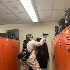 a man in a protective suit is spraying something in a locker room .