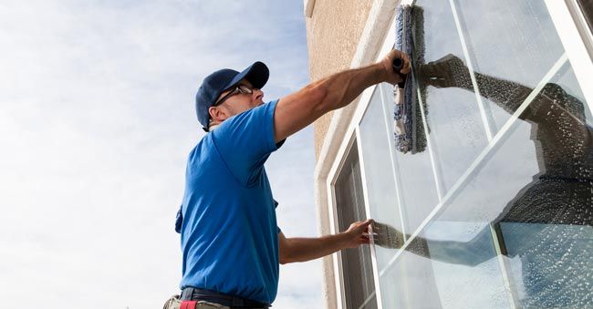a man in a blue shirt is cleaning a window with a squeegee 
