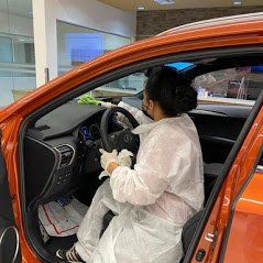 a woman in a protective suit is cleaning the interior of an orange car .