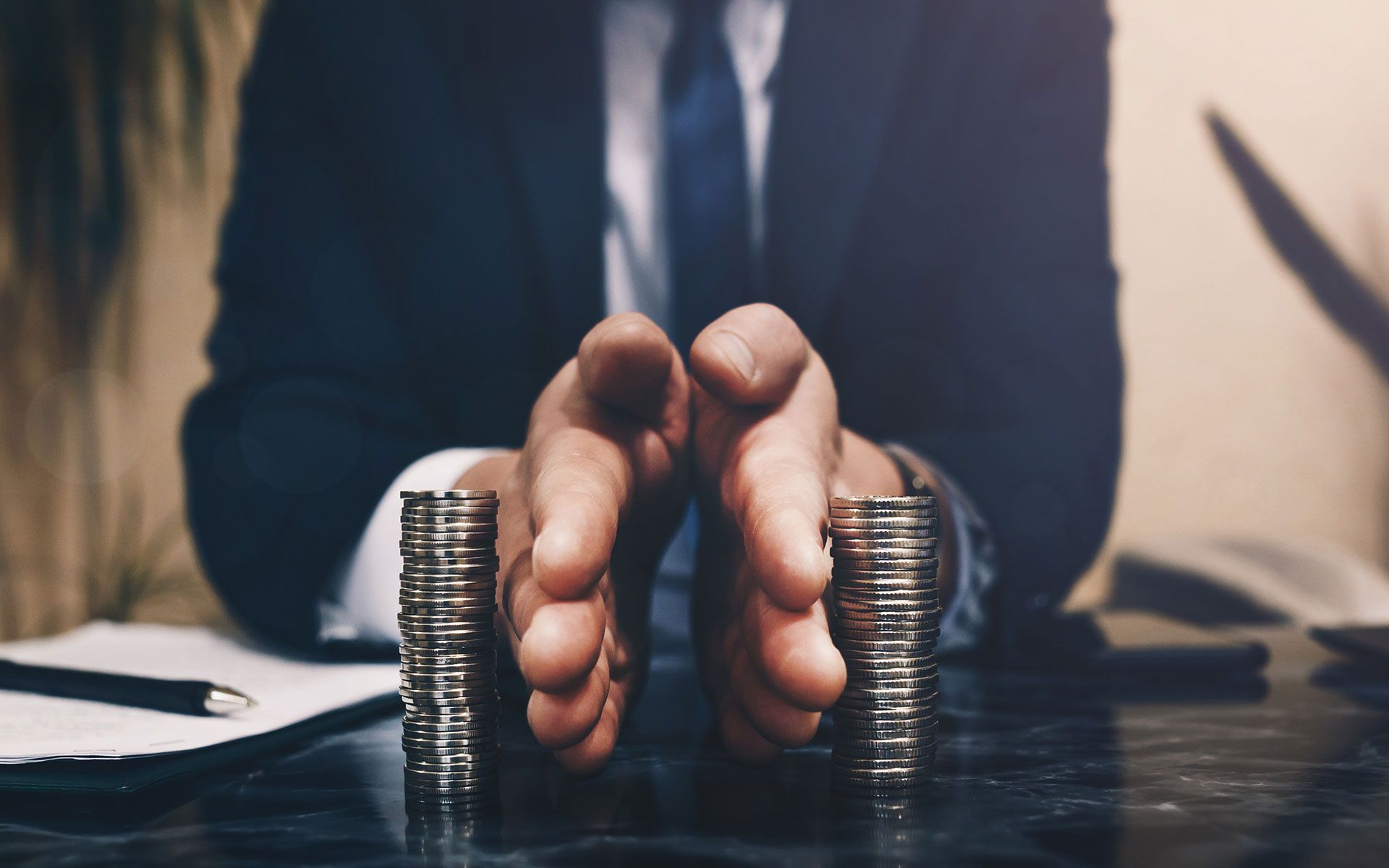 Person in a suit dividing two stacks of coins with their hands.
