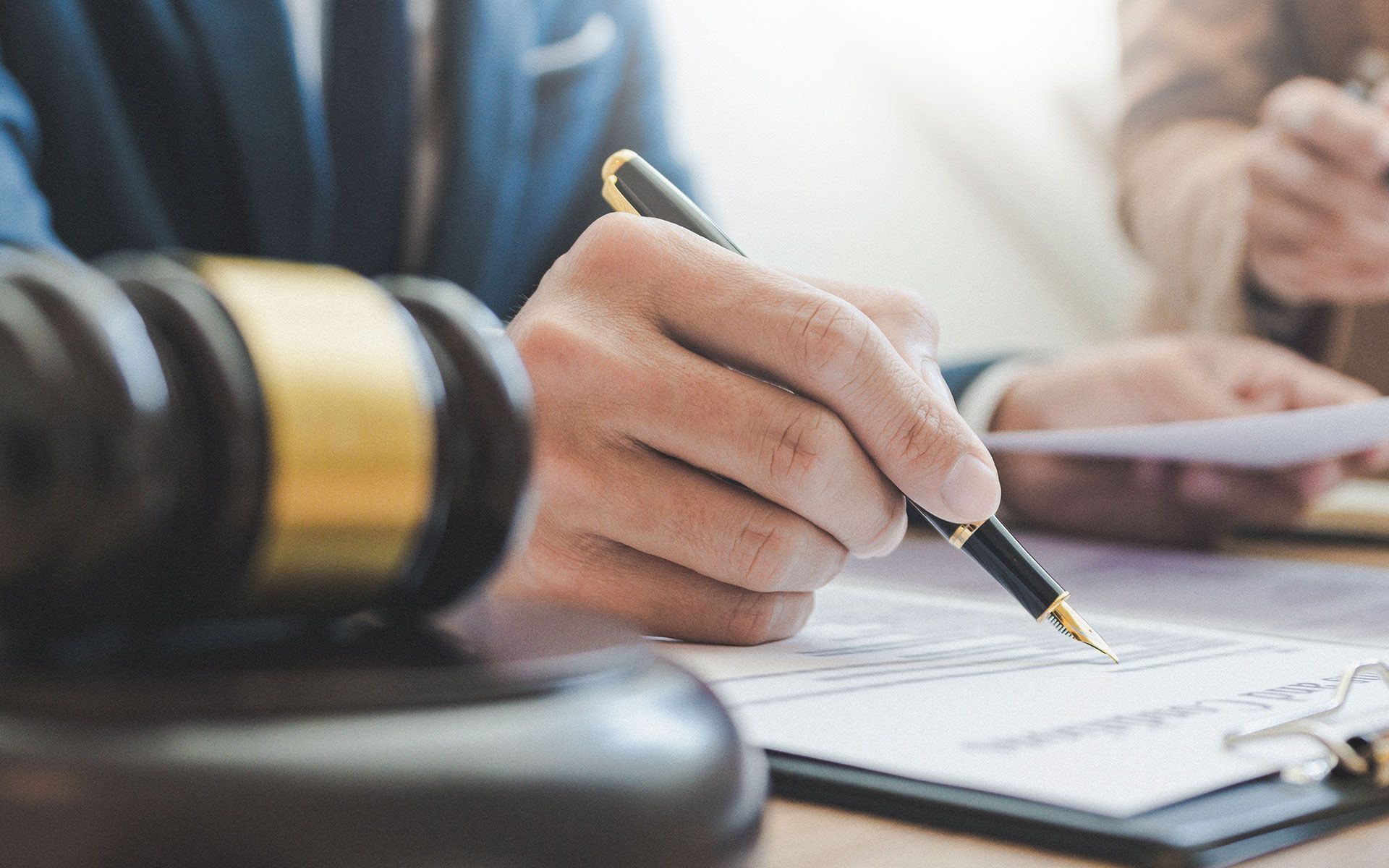 Hand signing legal documents with a gavel in the foreground.