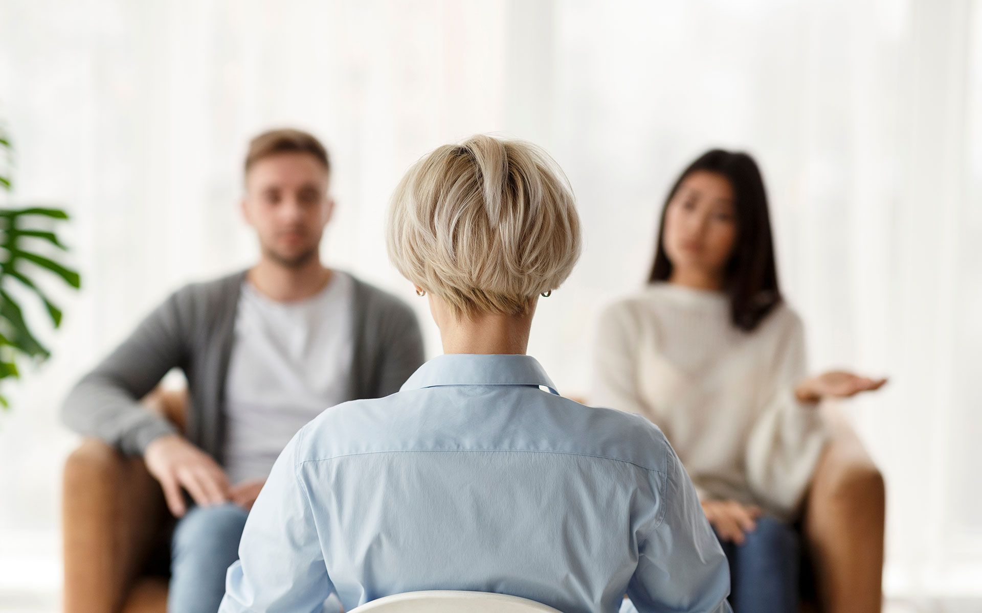 A therapist sits between a couple in a counseling session. The woman gestures and the man looks on.