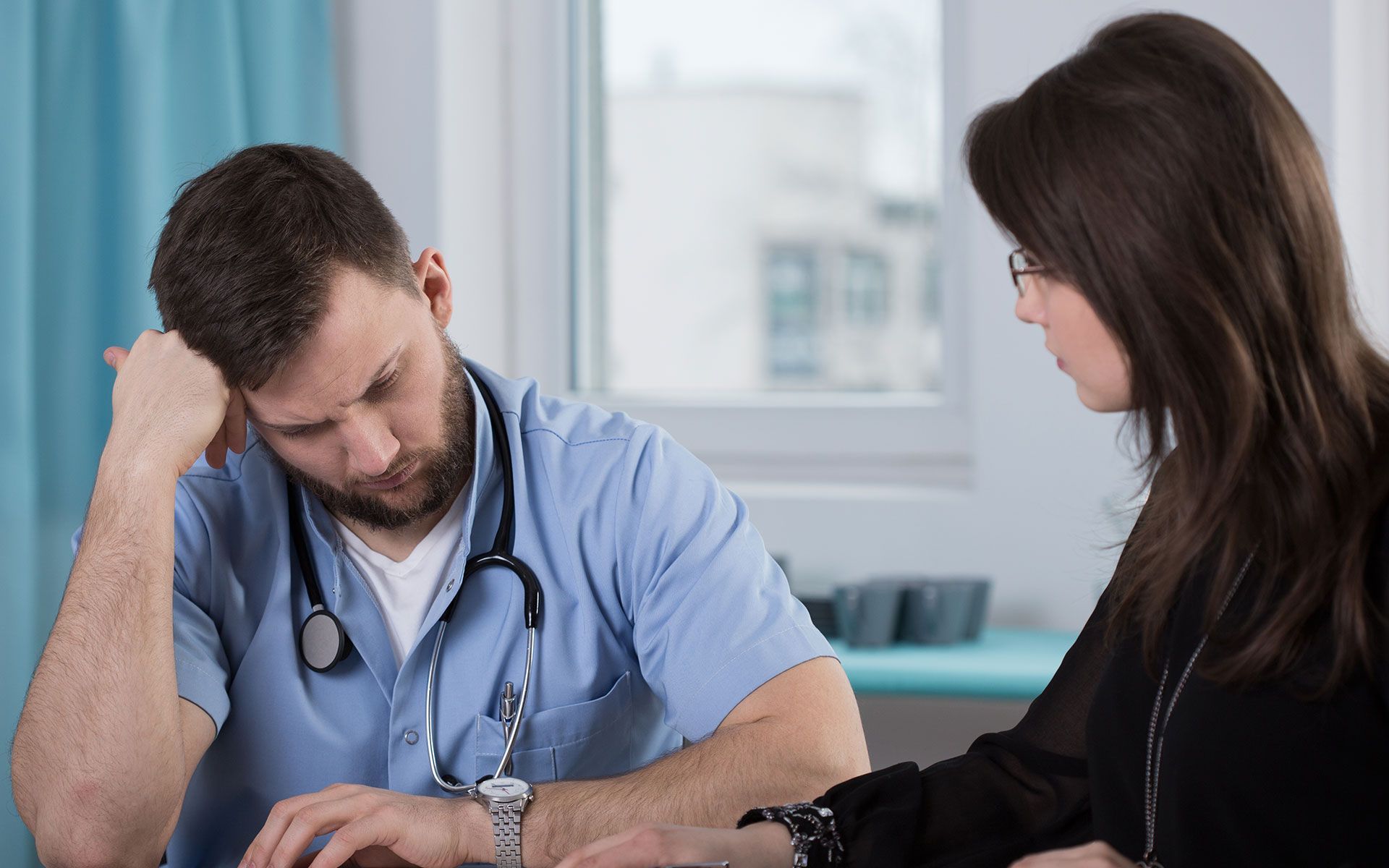 Doctor looking down, seemingly distressed, talking to a woman in a medical office.