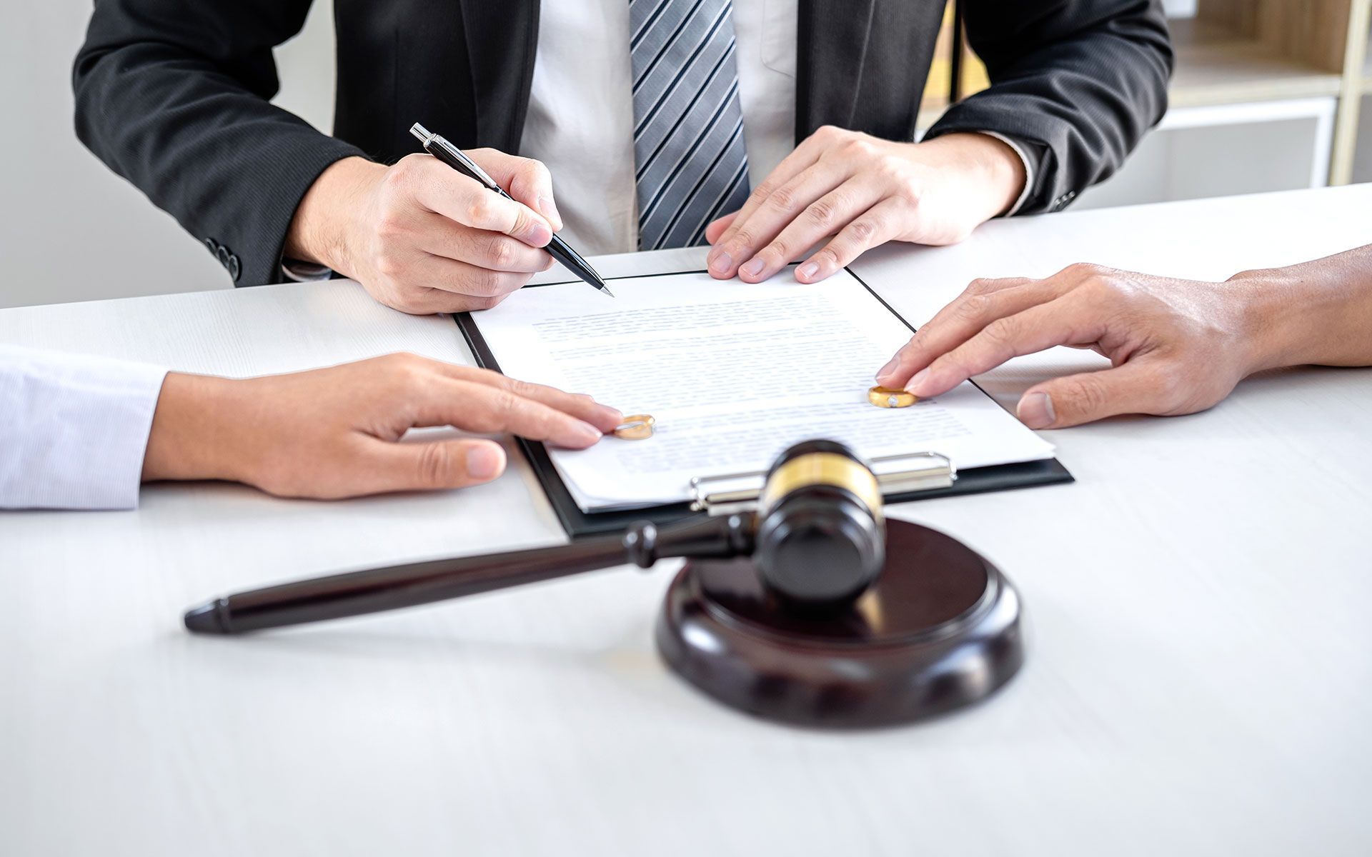 Lawyer signing documents with clients at a table, gavel in foreground.