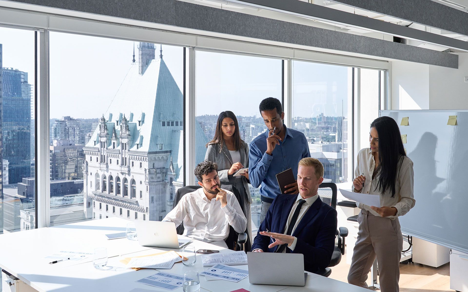 Business team in a modern office with city view, reviewing documents, brainstorming.