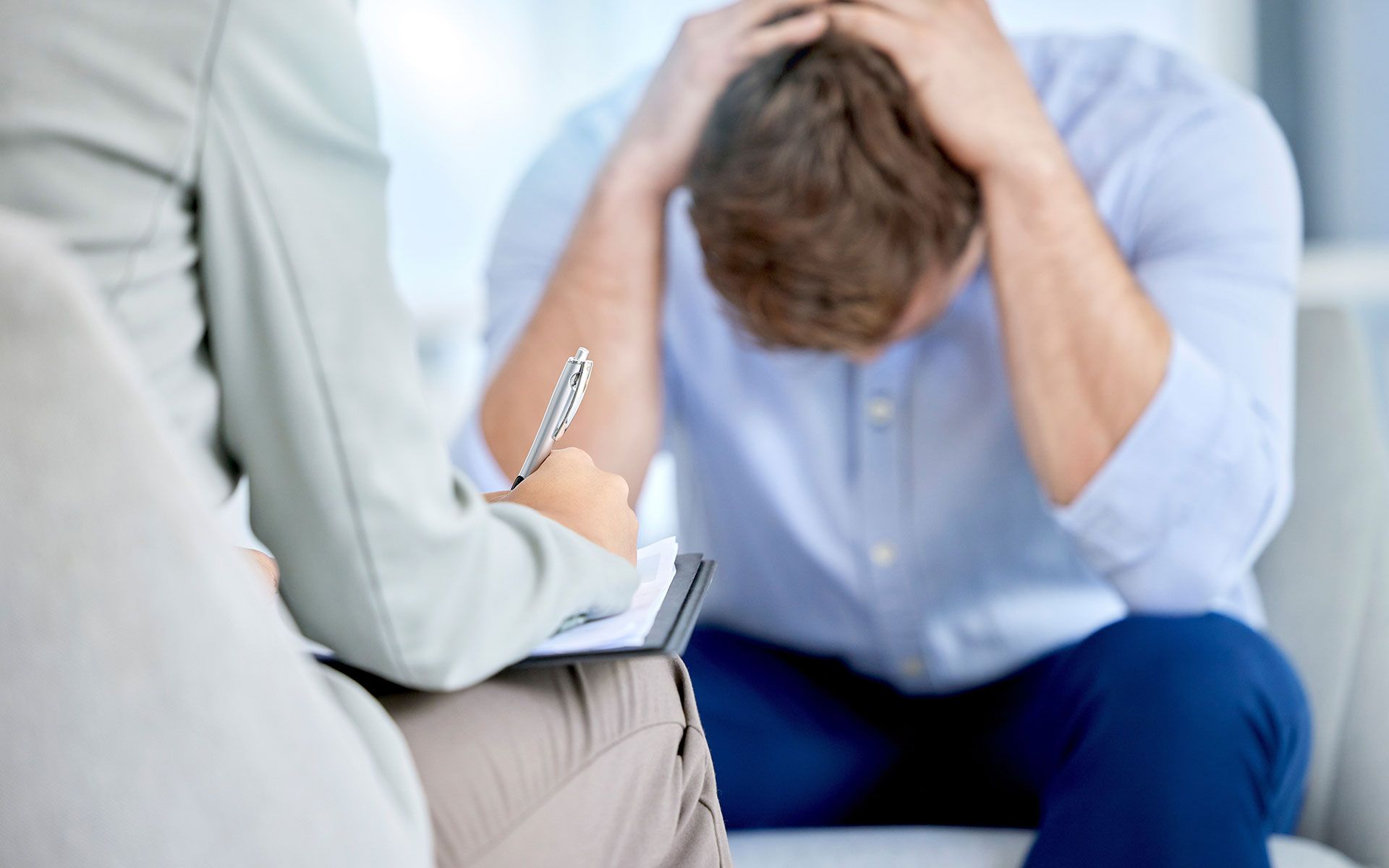 Man in distress with hands on head, consulting a therapist. Therapist takes notes.