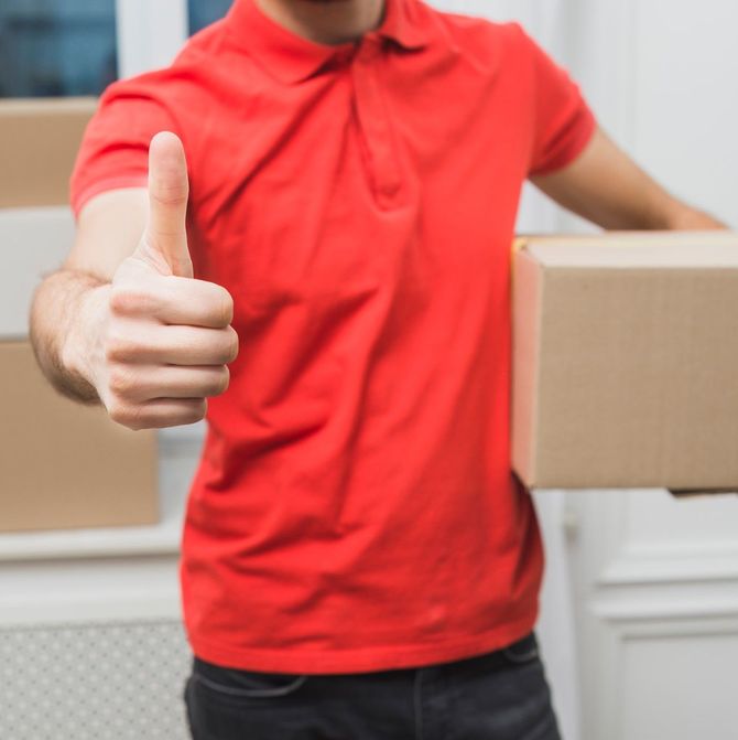 A man in a red shirt is holding a cardboard box and giving a thumbs up