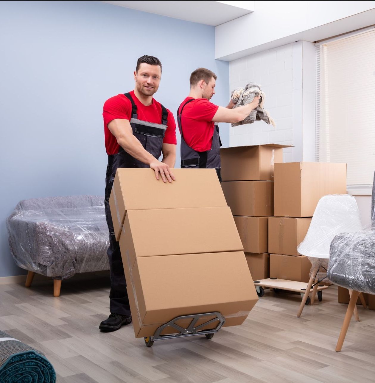 Two delivery men are carrying boxes and one is holding a clipboard.