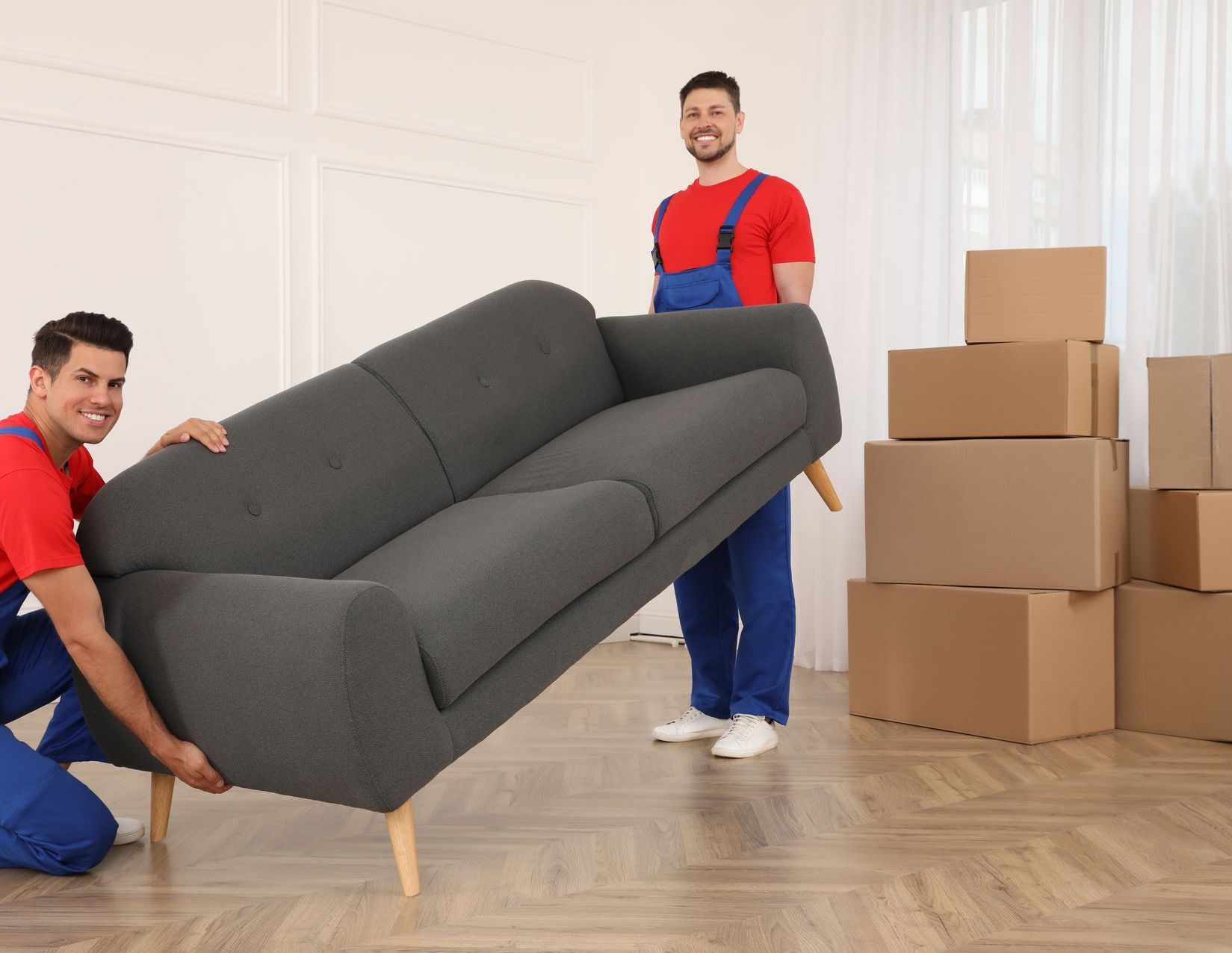 Two men are moving a couch in a living room.