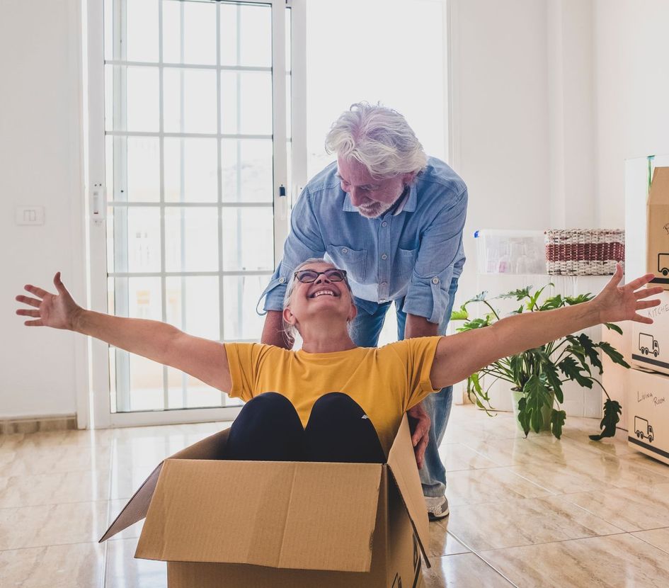 A woman is sitting in a cardboard box with her arms outstretched.