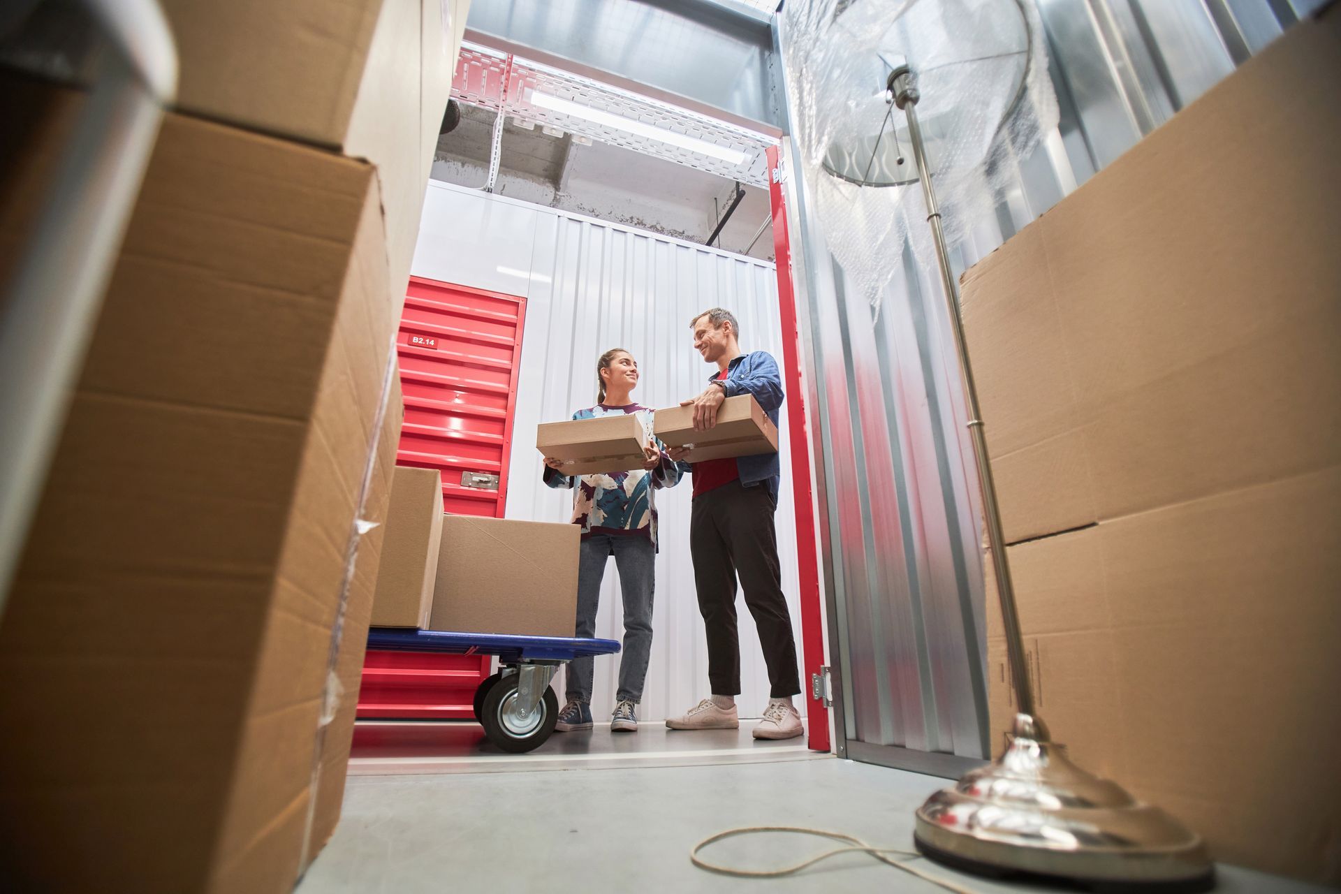 A man and a woman are carrying boxes in a storage unit.