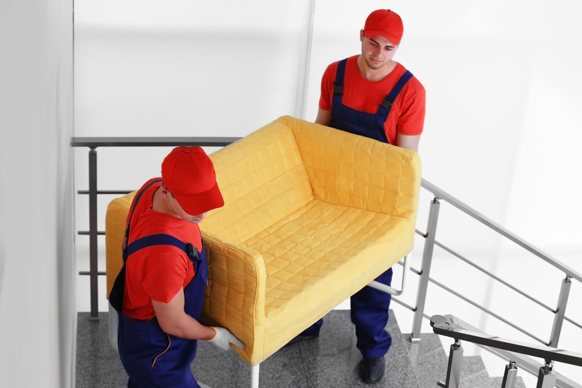 Two men are carrying a yellow couch up a set of stairs.