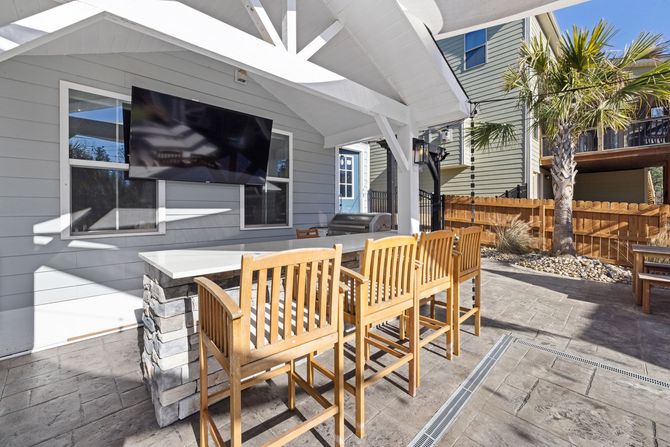 Outdoor patio with wooden chairs, stone table, and shaded seating beside a modern house