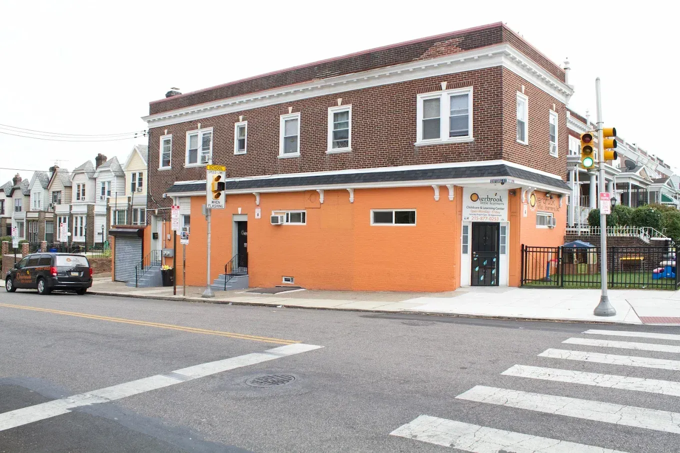 A two-story building with a brown patterned upper level and an orange ground floor on a street corner with a crosswalk.