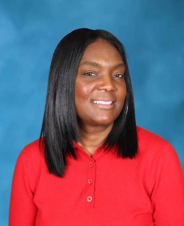 A smiling woman with shoulder-length dark hair wearing a red polo shirt, positioned against a solid blue background.