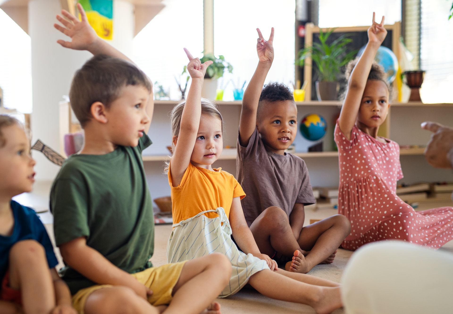A group of children sitting in a classroom, with three children raising their hands to answer a question.