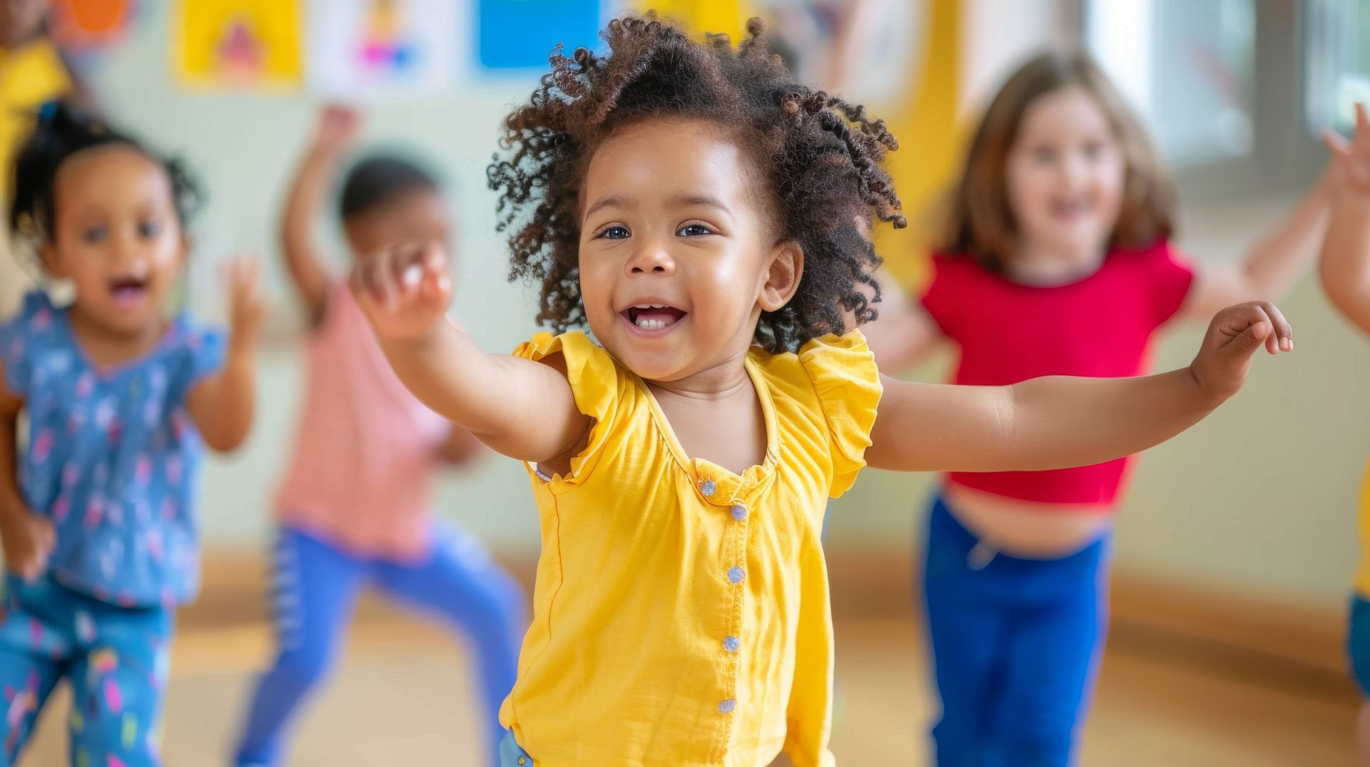 A group of children in a bright room smiling and dancing with arms outstretched.