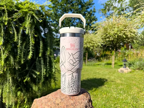 A stainless steel tumbler with a handle is sitting on top of a rock.