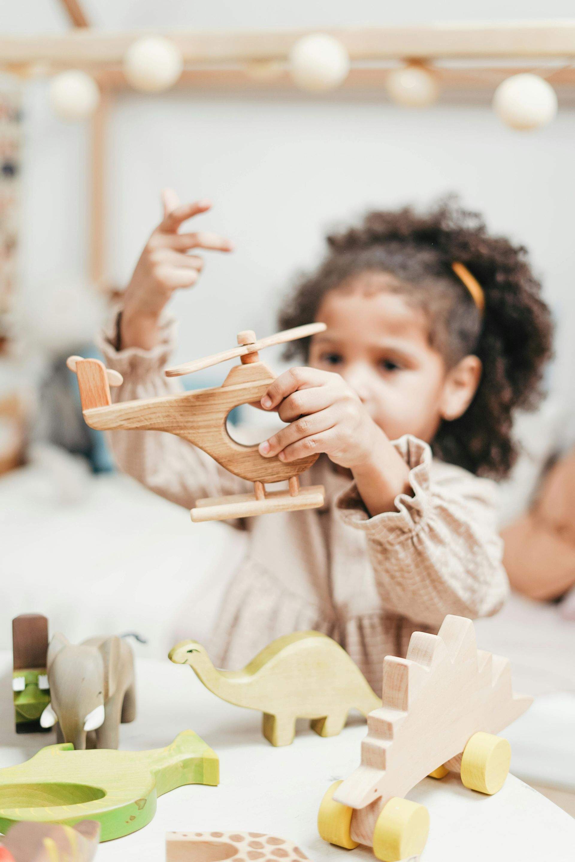 A little girl is playing with a wooden helicopter.