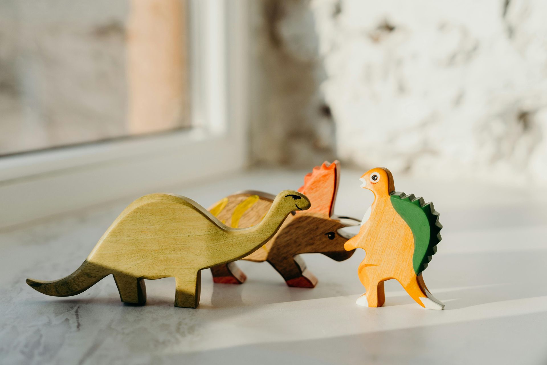 Three wooden dinosaurs are standing next to each other on a table.
