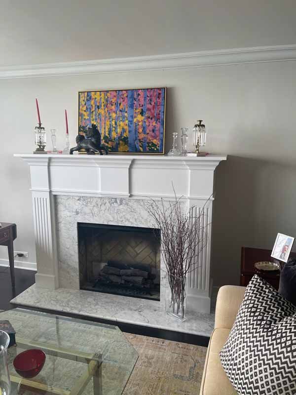 A living room with a fireplace and a painting on the mantle.