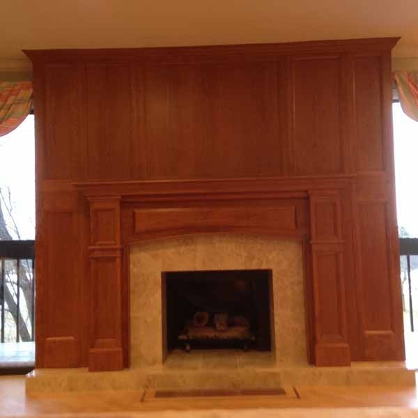 A fireplace with a wooden mantle in a living room next to a window.