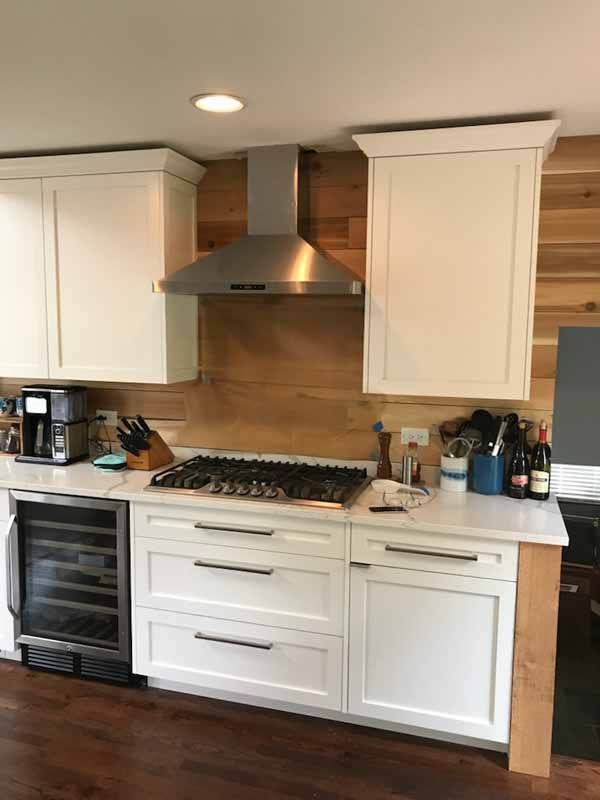 A kitchen with white cabinets , a stove , a refrigerator and a hood.