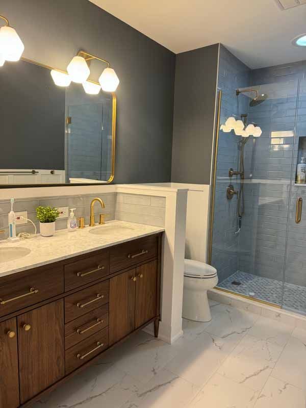 A bathroom with two sinks , a toilet , and a walk in shower.