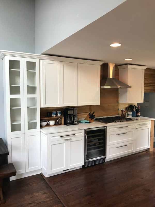 A kitchen with white cabinets , a stove , a refrigerator and a hood.