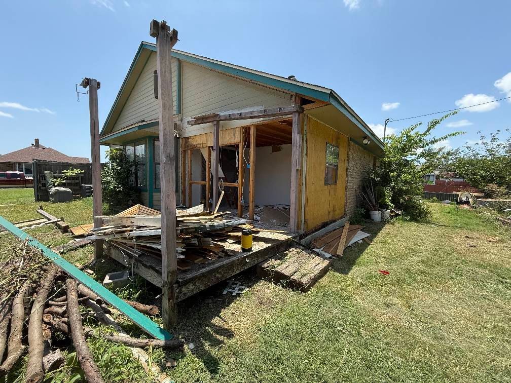 A small house is being demolished in the middle of a grassy field.
