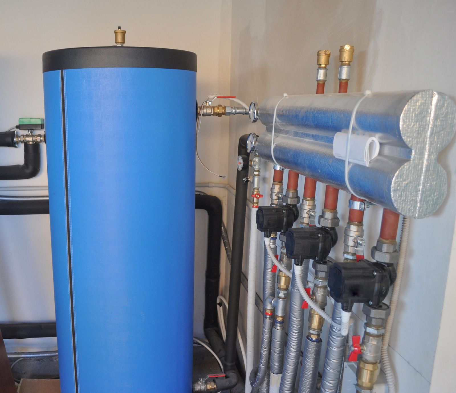 Blue water heater and manifold system with pipes in a utility room.