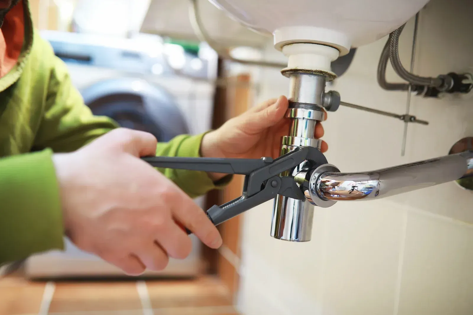 Person using pliers to tighten a pipe under a bathroom sink.