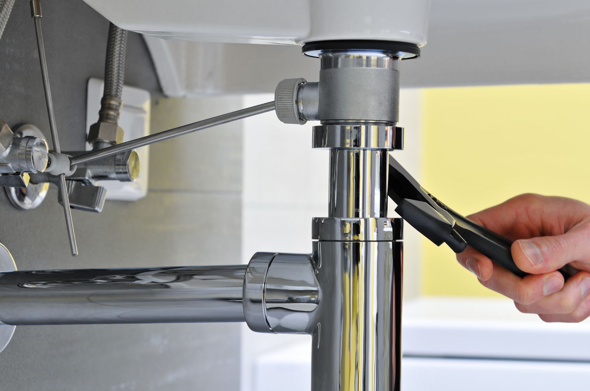 A person is fixing a sink pipe with a wrench.