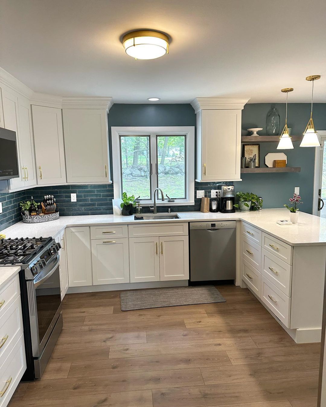 A kitchen with white cabinets , a stove , a sink , and a window.