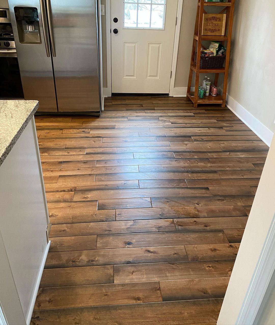 A kitchen with a wooden floor and a stainless steel refrigerator.