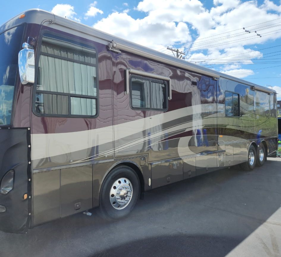 A large, brown and beige recreational vehicle parked on asphalt against a blue sky.