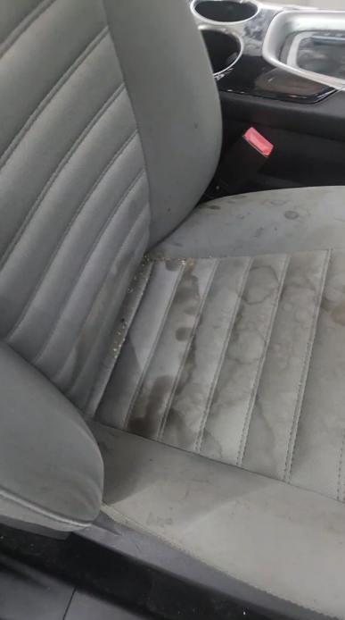 Dirty gray car seat with dark stains. Cup holders visible.