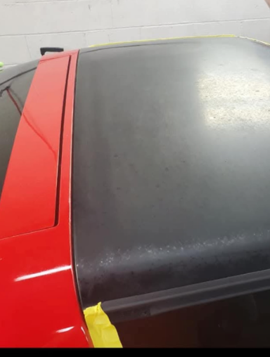 Red car roof being painted black; yellow tape used to mask the area.