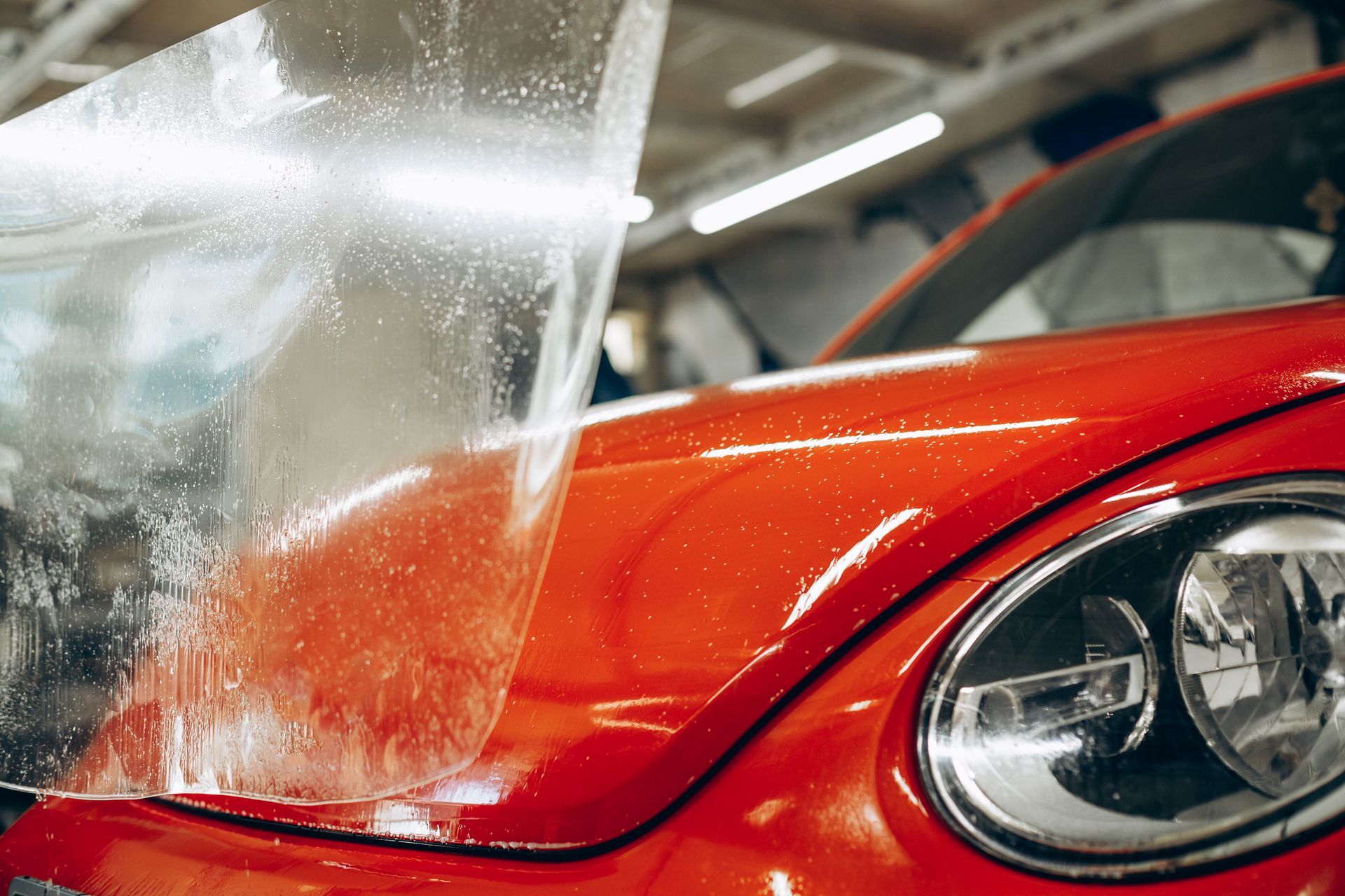 Clear protective film being applied to a shiny red car's hood.