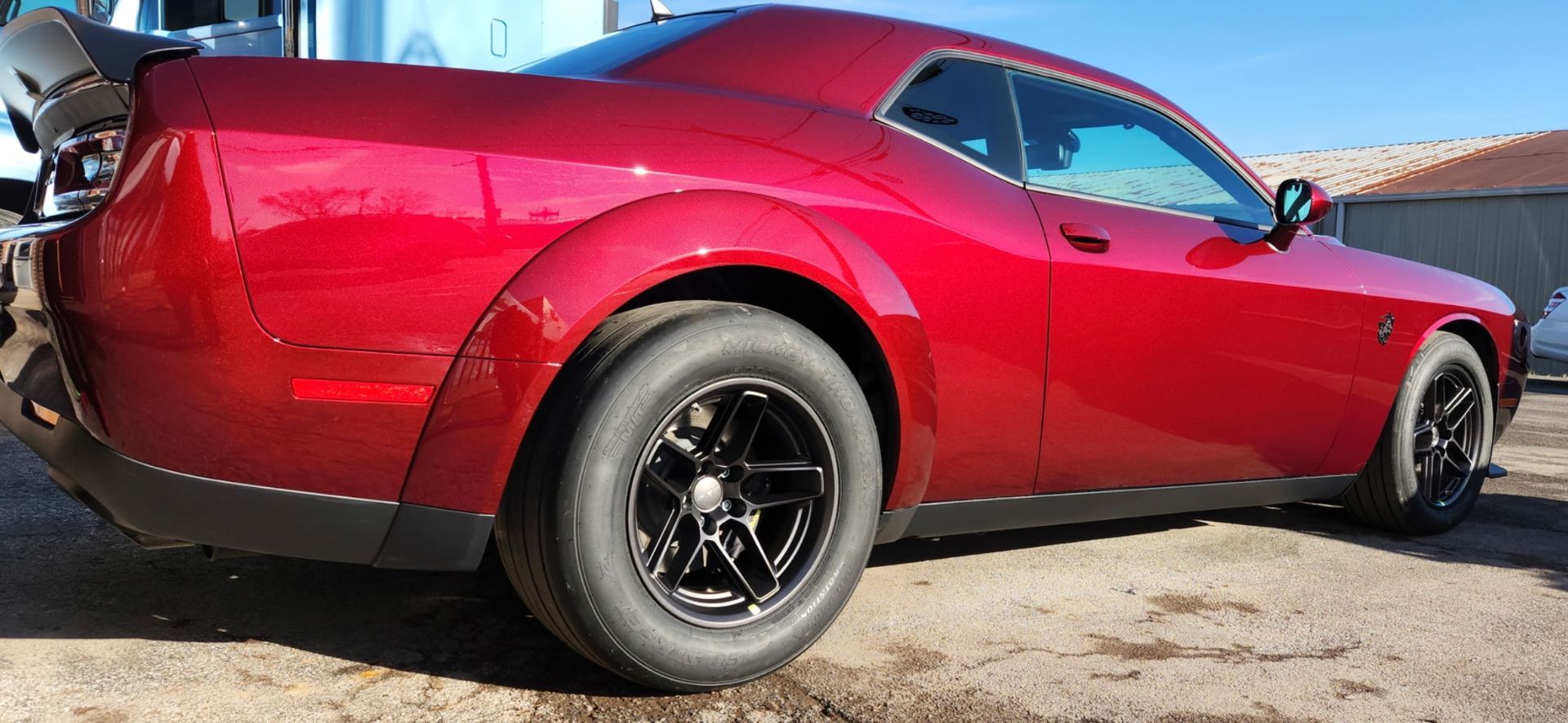 Red Dodge Challenger with black wheels parked outside on a sunny day.